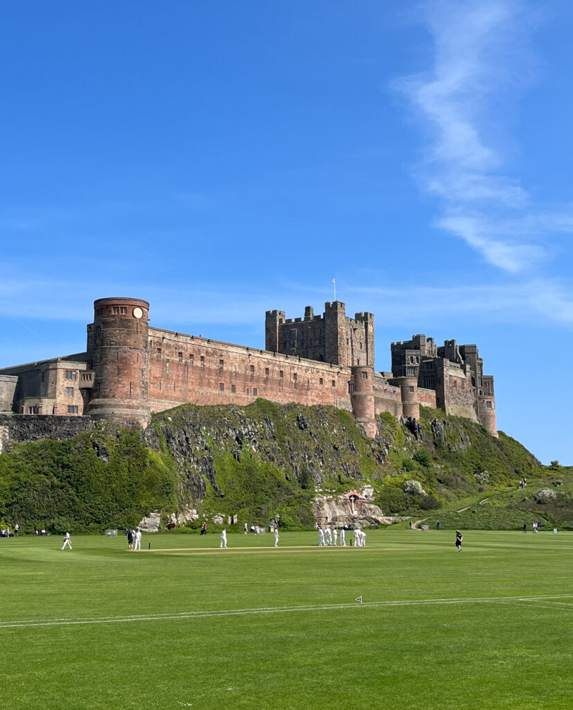 A view of Bamburgh Castle with a cricket match taking place in the foreground. 