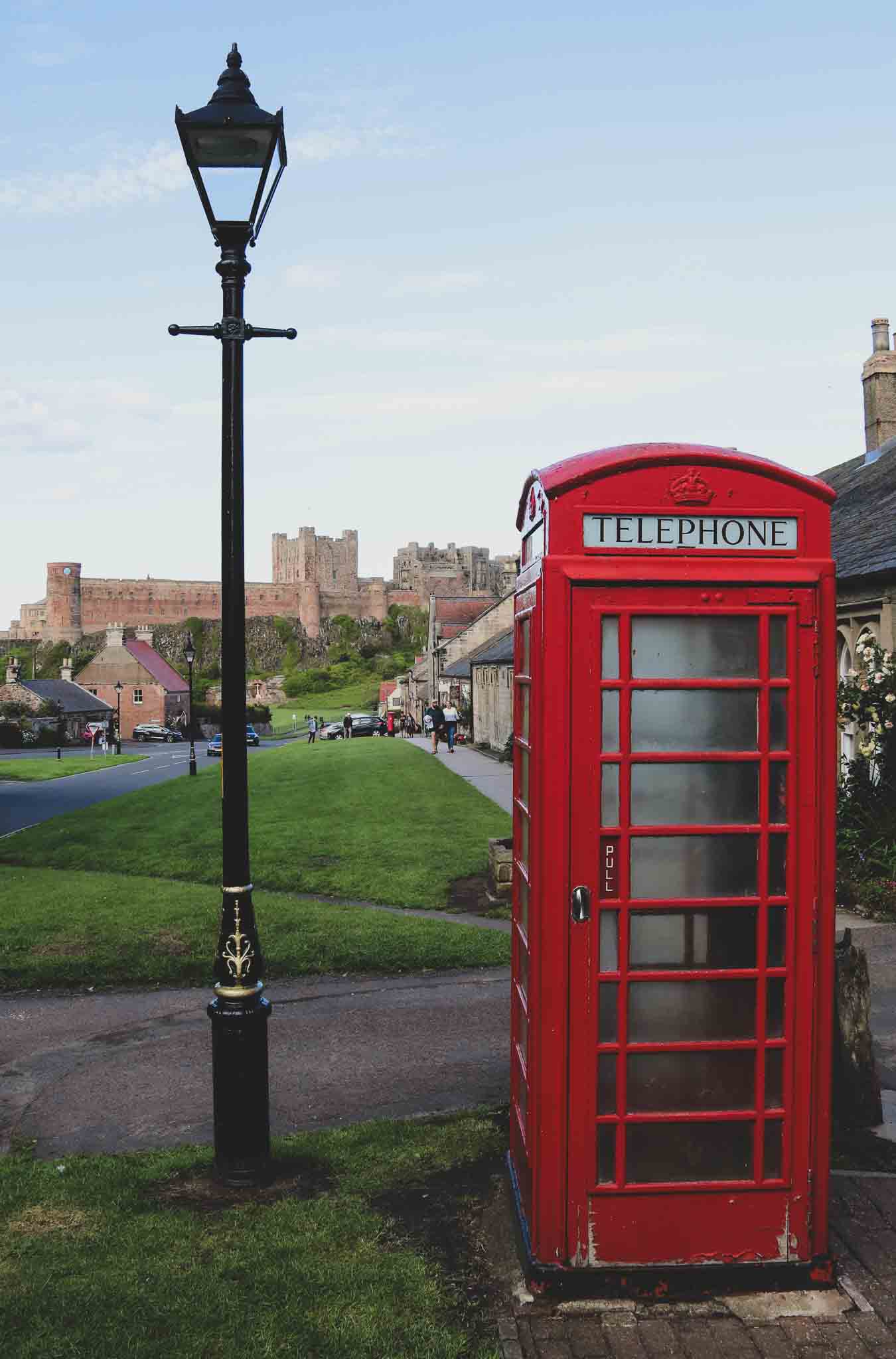 A view of Bamburgh Castle from the village square. A telephone box and a vintage lamppost stand in the foreground. 